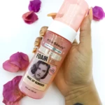 Bote de removedor de maquillaje hidratante Kiss Beauty Real Fresh Foam, sostenido en mano con flores.
