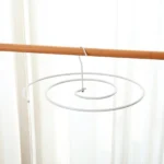 Gancho en espiral blanco colgando de una barra de madera contra un fondo de cortina clara.