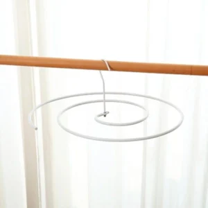 Gancho en espiral blanco colgando de una barra de madera contra un fondo de cortina clara.