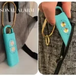 Alarma de seguridad de autodefensa color turquesa con dos luces LED en un llavero de carabina dorado.