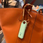 Alarma de seguridad de autodefensa cuelga de bolso de cuero naranja con hebilla dorada.