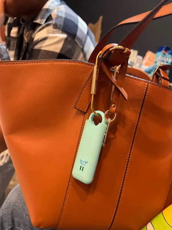 Alarma de seguridad de autodefensa cuelga de bolso de cuero naranja con hebilla dorada.
