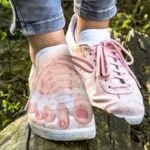 Separador de silicona para dedos en zapatillas rosadas sobre tronco de madera.