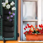 Bolsa para plantar vertical de fieltro negro con flores blancas y moradas junto a maceta de tulipanes rojos.