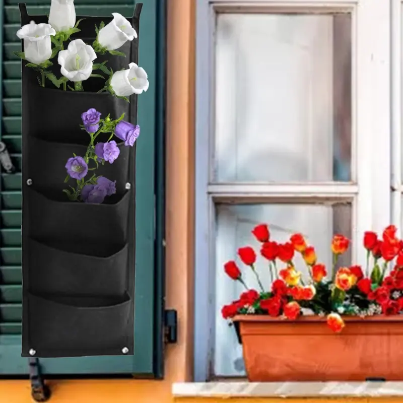Bolsa para plantar vertical de fieltro negro con flores blancas y moradas junto a maceta de tulipanes rojos.