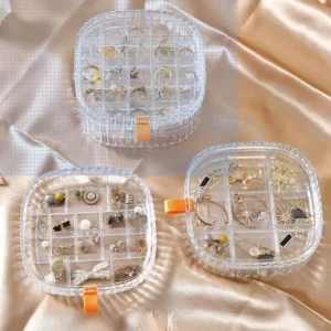 Organizador de joyero transparente con varios compartimentos exhibiendo anillos, aretes y collares dorados.