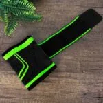 Muñequera de compresión alta negra con detalles verdes, diseño ergonómico para soporte deportivo.