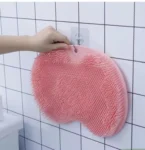 Tapete de baño rosa con ventosas antideslizantes, colgando de un gancho en una pared de azulejos.