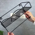 Estante de pared negro con soporte, sujetado por manos, ideal para organizar objetos.