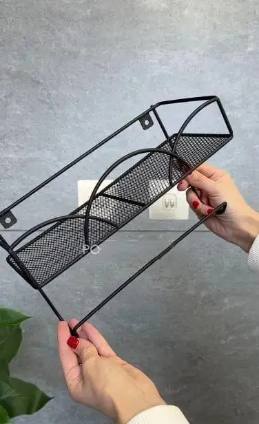 Estante de pared negro con soporte, sujetado por manos, ideal para organizar objetos.