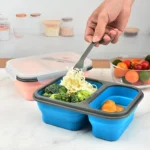 Porta comida plegable azul y gris con brócoli, fideos y croissants, ideal para llevar.