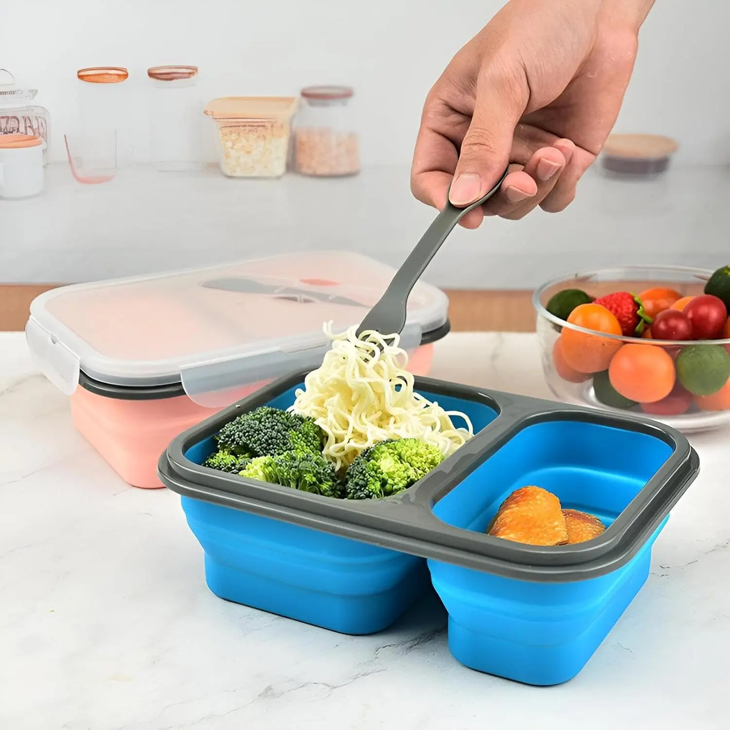 Porta comida plegable azul y gris con brócoli, fideos y croissants, ideal para llevar.