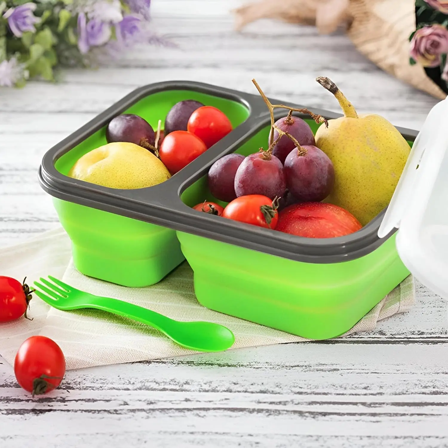 Porta comida plegable verde con frutas y tenedor, ideal para almuerzos.