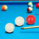 Juego 3 bolas de billar Carambola de lujo: 2 blancas y 1 roja sobre mesa azul con taco.