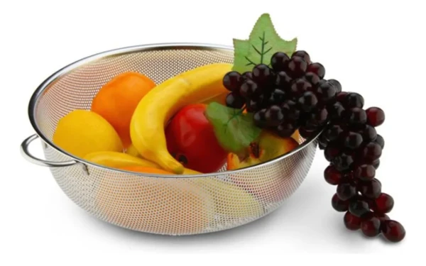 Colador escurridor metálico con frutas: banano, naranja, limón y uvas rojas.