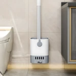 Cepillo de baño blanco y gris con soporte, junto a inodoro y mueble de baño.