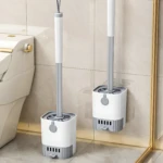 Cepillo de baño blanco y gris con soporte para colgar en pared junto a inodoro.