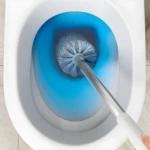 Cepillo de baño limpiando taza sanitaria con agua azul.