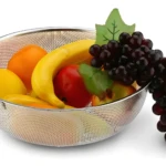 Colador escurridor metálico de 22.5cm lleno de frutas: banano, uvas, naranja y más.