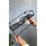 Estante de pared negro con soporte para colgar objetos en pared de textura gris.