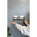 Estante de pared negro con dos jabones y manos ajustando soporte.