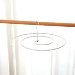 Gancho en espiral blanco colgando de barra de madera frente a cortina blanca