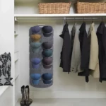 Colgador vertical de gorras de 14 compartimentos en closet con abrigos colgados y cestas de mimbre arriba.