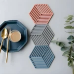 Posa vasos de silicona hexagonales apilados, con plato azul, cubiertos dorados y vaso con bebida.