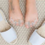 Separador de silicona para dedos de pies con sandalias blancas sobre alfombra.
