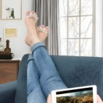 Pie descansando con separadores de silicona para dedos y tableta, mientras mira por la ventana.