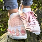 Separador de silicona para dedos del pie en zapatillas rosadas sobre tronco de árbol.