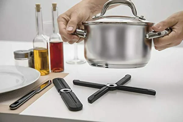 Salva mantel moderno negro, con ollas de acero inoxidable y botellas de aceite y vino.