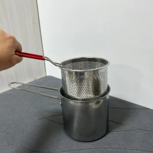 Olla freidora de acero inoxidable con escurridor de aceite y asas rojas, vista de cerca.