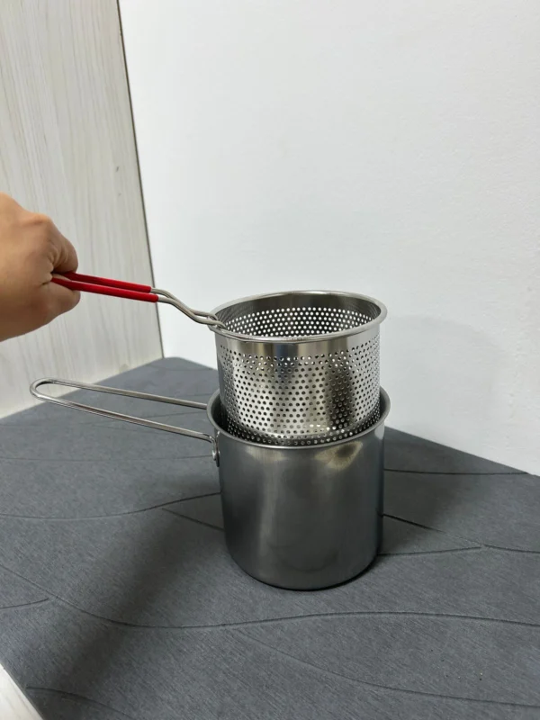 Olla freidora de acero inoxidable con escurridor de aceite y asas rojas, vista de cerca.