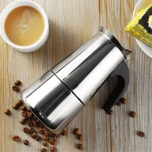 Cafetera italiana plateada para espresso de 6 tazas, con taza de café y granos sobre mesa de madera.