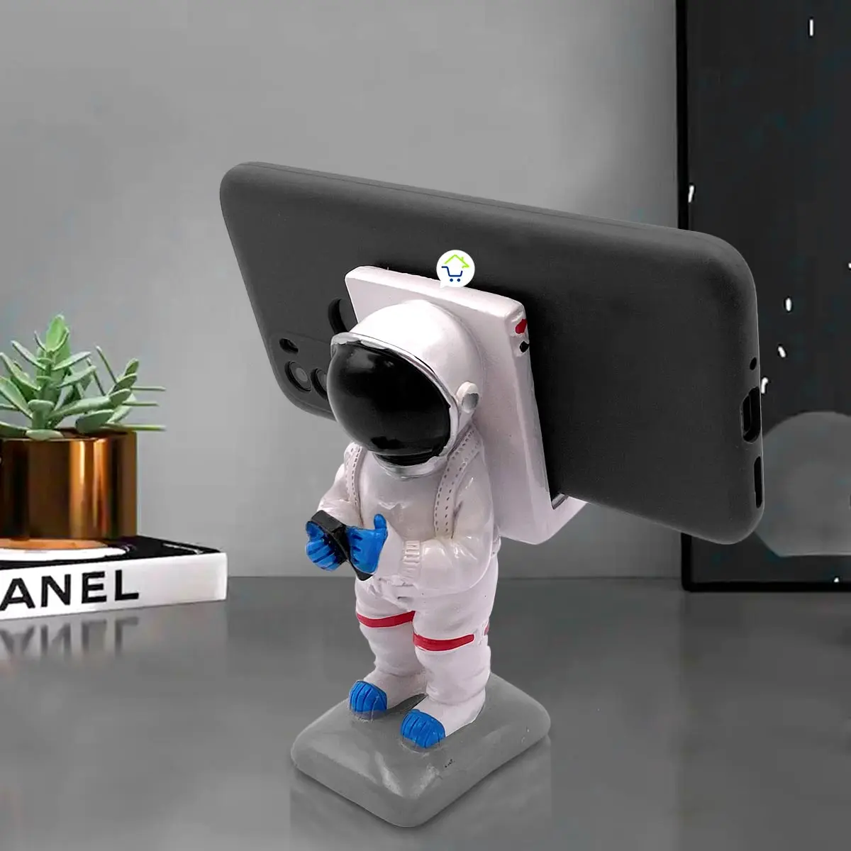 Soporte celular astronauta blanco con tablet en mano, base gris sobre mesa.