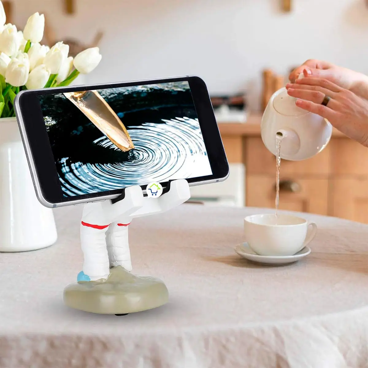 Soporte de celular astronauta SCah01 vertiendo agua en taza, con tulipanes blancos.