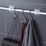 Barra ajustable para cortina sin clavos sosteniendo bolso, cinturón y toalla de gris.