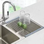 Escurridor enrollable de acero inoxidable para secar platos sobre el lavaplatos, con limones y vasos.