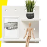 Repisa organizador de pared perforada con cuadro y muñeco articulado.