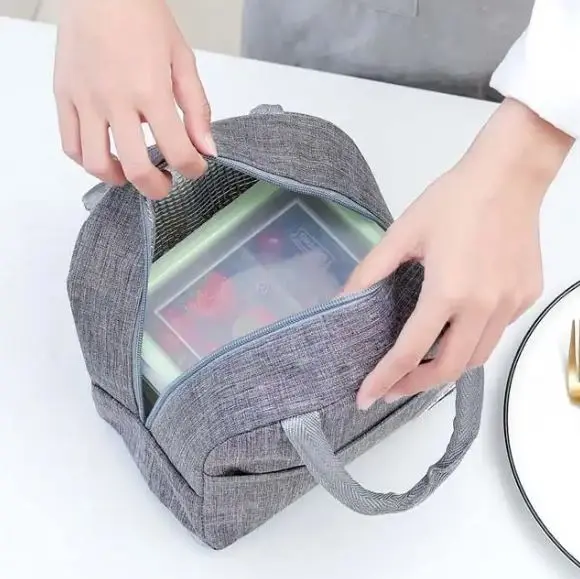 Lonchera térmica gris con contenedor transparente y asas, ideal para llevar alimentos.