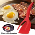 Espátula pinza roja para freír huevos y tocineta fácilmente en sartén.