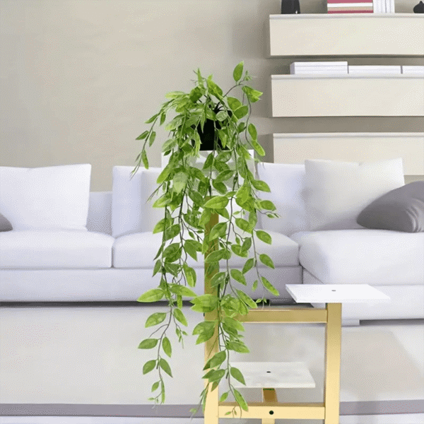 Planta colgante hiedra artificial en matero moderno sobre mesa dorada junto a sofá blanco.