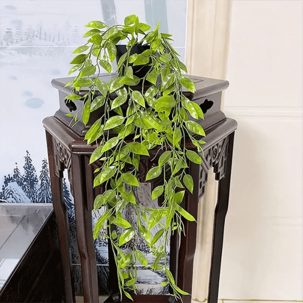 Planta colgante hiedra artificial sobre mueble tallado oscuro con paisaje de fondo.