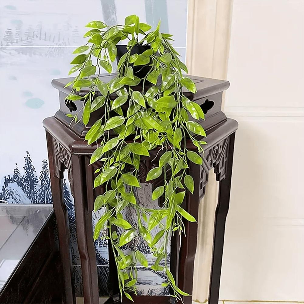 Planta colgante hiedra artificial sobre mueble tallado oscuro con paisaje de fondo.