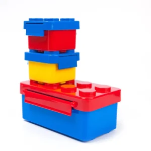 Fiambrera lonchera tipo Lego, apilable, roja y amarilla con tapas azules.