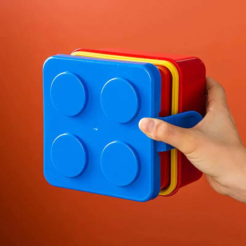 Fiambrera lonchera Lego azul con tapas rojas y amarillas, sujetada por mano.