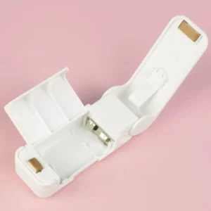 Mini selladora de bolsas blanca abierta mostrando compartimiento para baterías sobre fondo rosa.