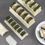 Molde con ranuras para cortar sushi, mostrando rollos de sushi recién hechos en moldes y listos para servir.