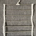 Perchero colgador con 5 barras metálicas y gancho giratorio blanco para pantalones.